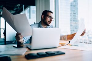 Profissional concentrado verificando documentos financeiros e dados no notebook sobre divergência entre laudos periciais.