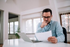 Homem sério com expressão concentrada analisando documento em papel sobre nulidade de laudo pericial.